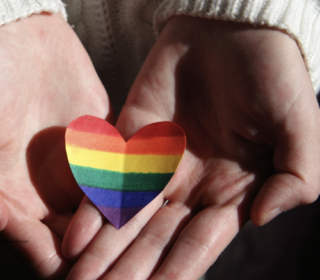 A photo showing a pair of hands holding a heart in rainbow colours