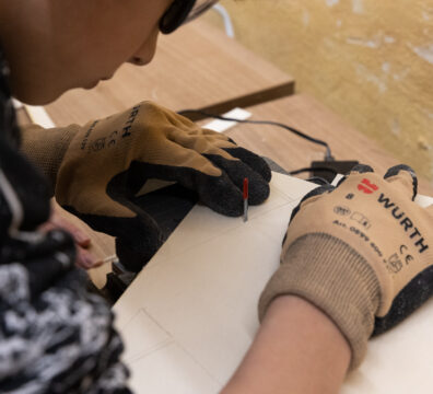A close up of a child's hand in safety gloves working with wood