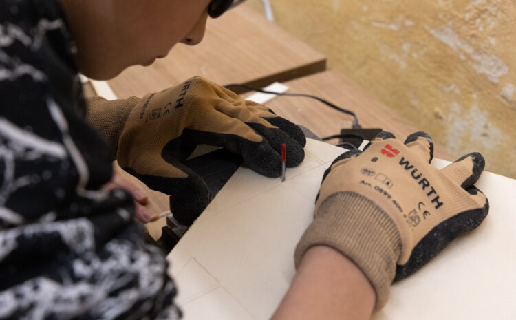 A close up of a child's hand in safety gloves working with wood