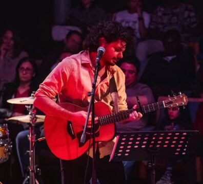 A photo showing a guitarist in live concert with the audeince behind him