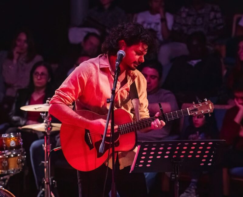 A photo showing a guitarist in live concert with the audeince behind him